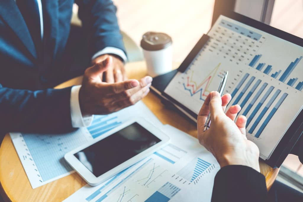Two Hands Pointing Towards iPad Showing A Bar Chart- dynamics 365 financial management
