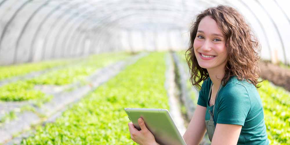 Woman smiling while checking on a field of crops in a greenhouse