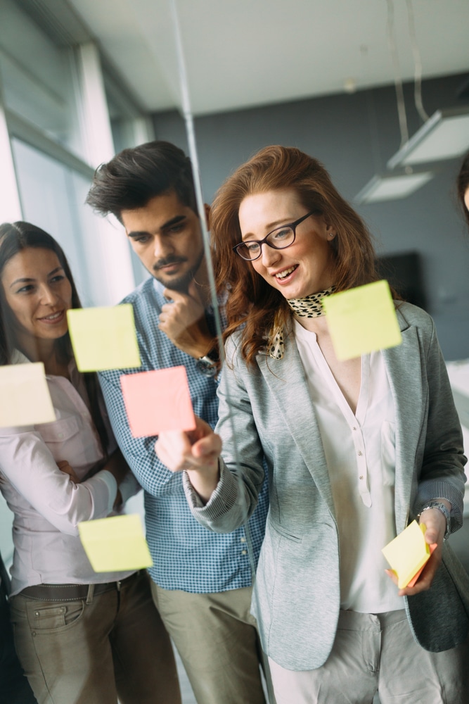 Woman writing on sticky notes next to her coworkers