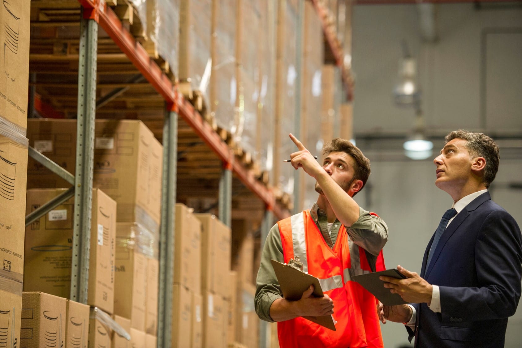 Worker and businessman with digital tablet and clipboard in warehouse