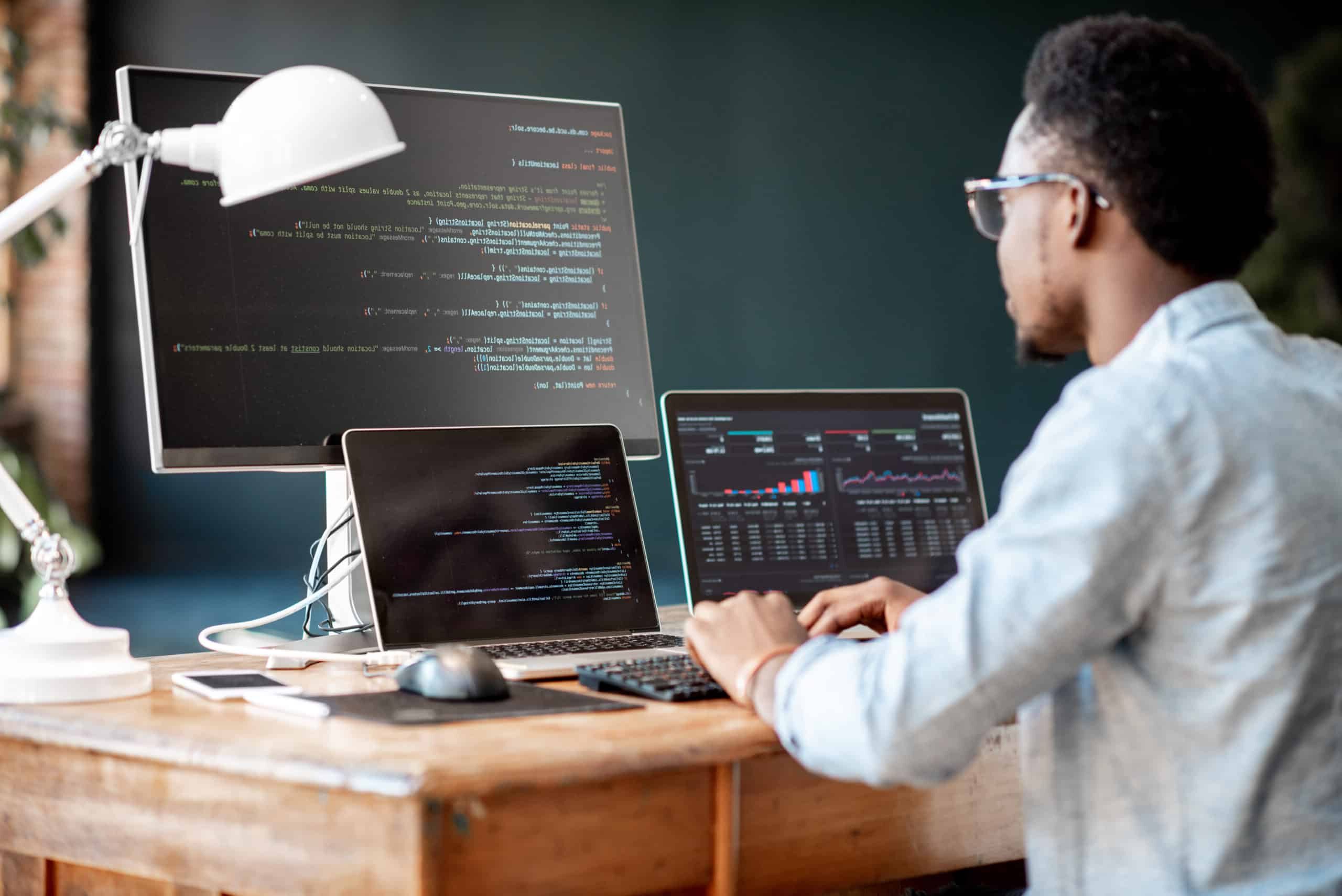 man writing code on computer and laptop