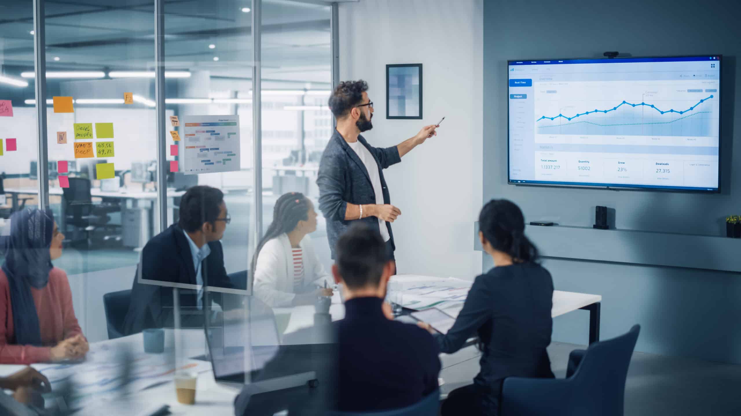 team in a meeting room, man points at screen with charts