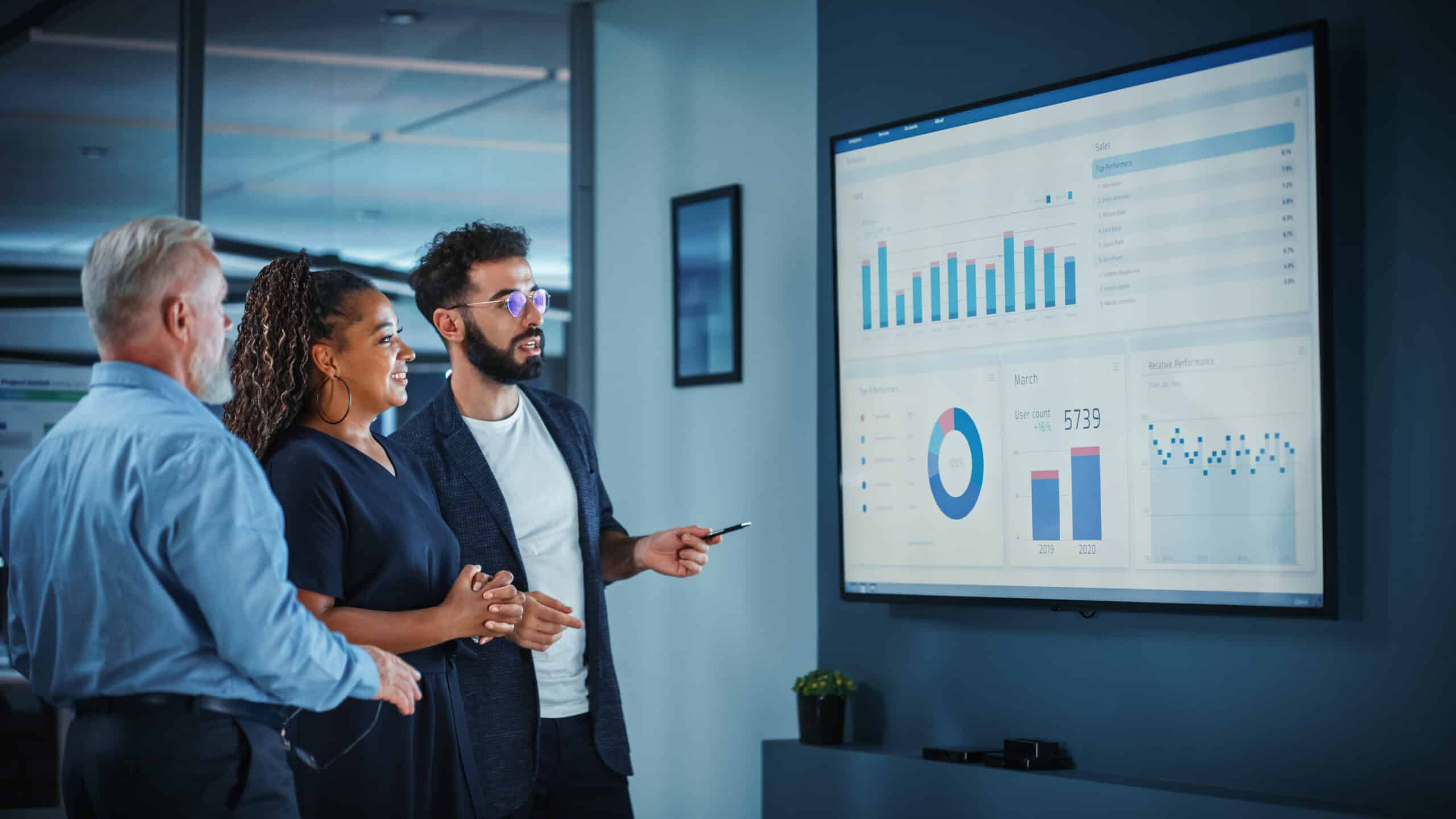 man showing graphs on screen to 2 other people