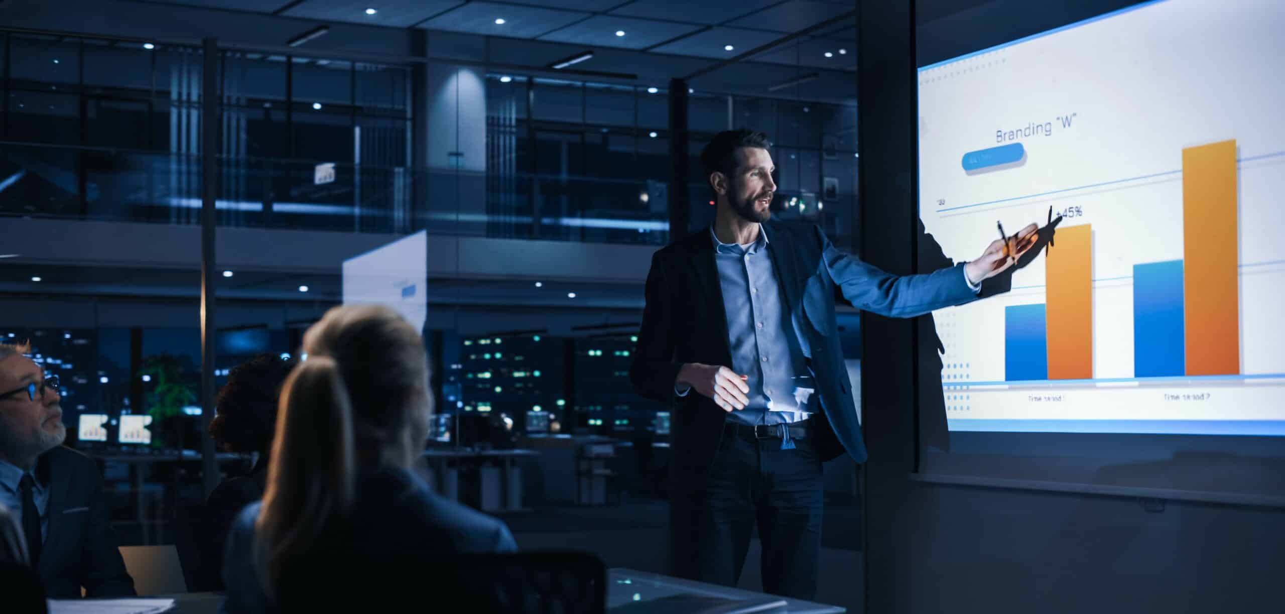 man in business meeting pointing to screen with graphs