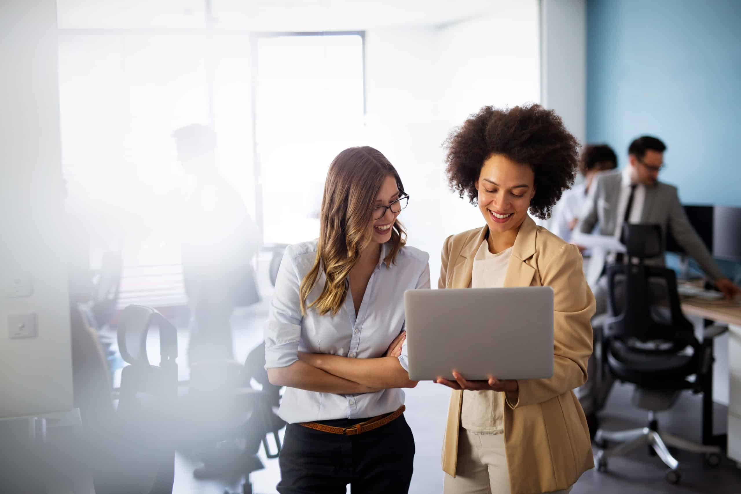 Businesswoman in a work setting showing a colleague how easy Dynamics 365 Business Central is to use on her laptop.