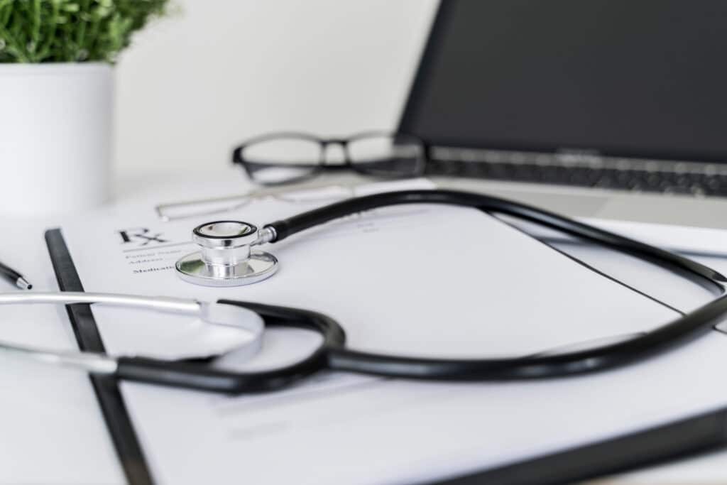 Stethoscope, Rx prescription and laptop on doctor desk in office.