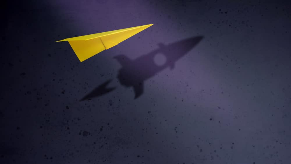 paper airplane with the shadow of a rocket ship