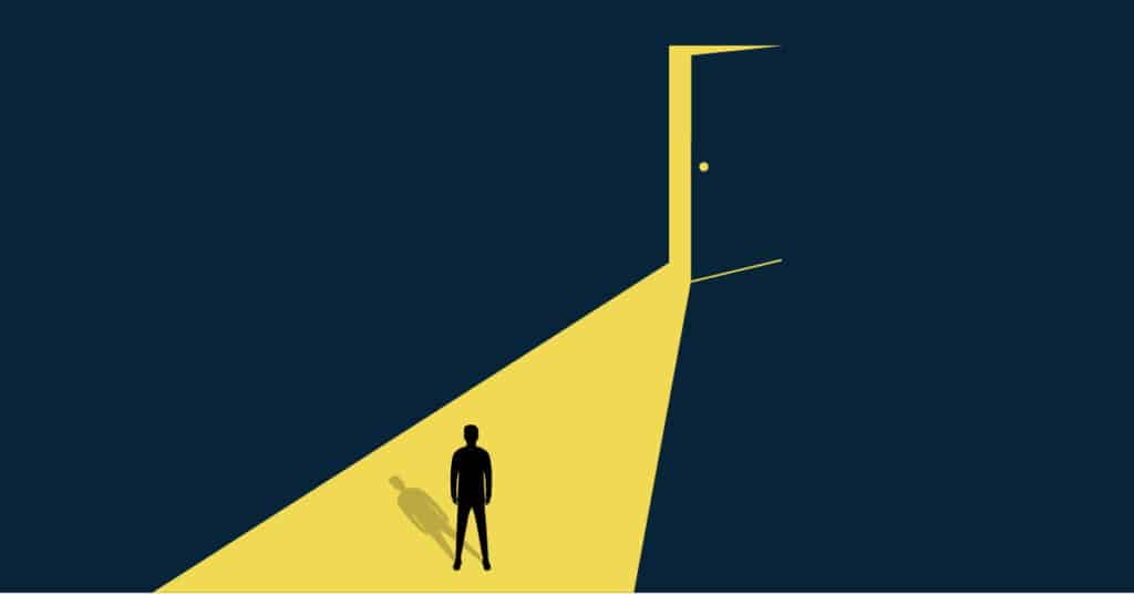 Man standing in a dark room looking at an open door that is flooding his path with light